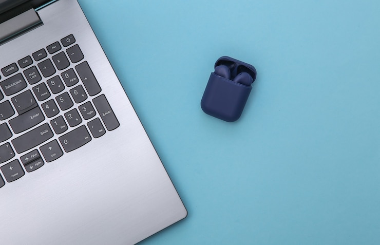 Foto portátil y auriculares inalámbricos con estuche cargador sobre fondo azul. vista superior