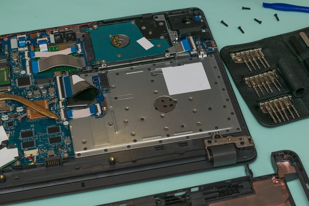 Un portátil desmontado y un conjunto de herramientas de reparación sobre una mesa azul.