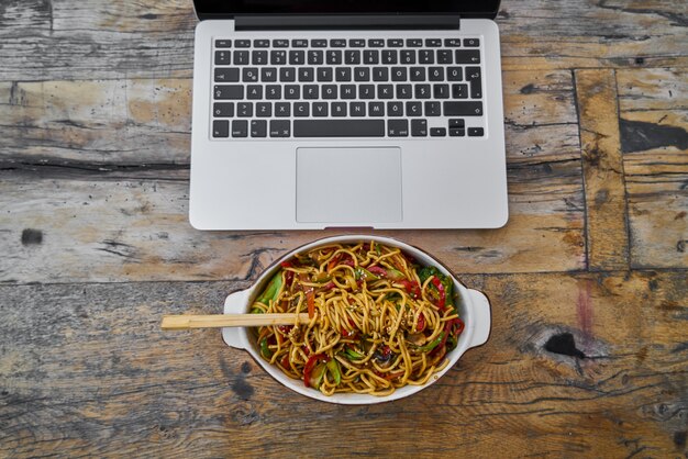 Portátil y fideos en la mesa de madera