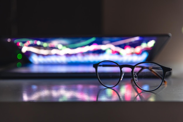 Portátil con gráficos y estadísticas y gafas sobre la mesa.