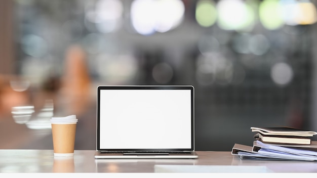 Portátil con pantalla en blanco blanco sobre mesa blanca con taza de café y archivo de documentos. Interior del hogar u oficina