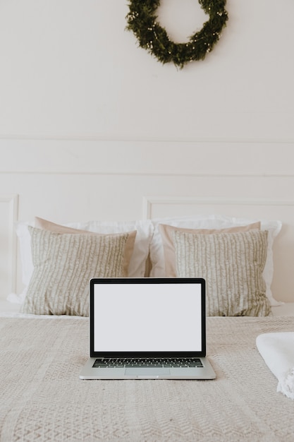 Portátil de pantalla en blanco en la cama con almohadas y ropa de cama