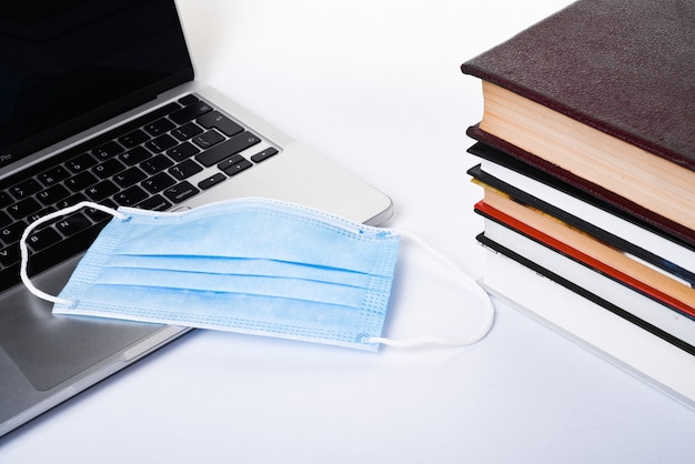 Foto portátil, pila de libros y máscara médica en blanco