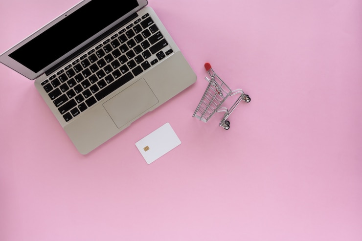 Foto portátil con tarjeta de crédito en blanco y mini carrito de compras sobre fondo rosa