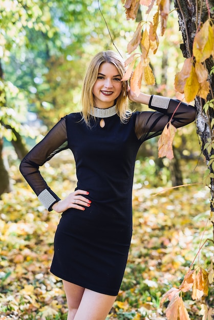 Porteait feminino no parque outono. Beaurtiful mulher de vestido preto posando com árvores amarelas