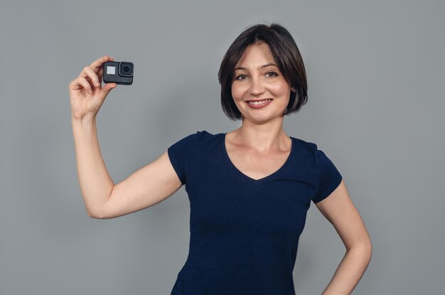 Porteiro de mulher com cabelo preto curto segurando uma câmera com uma mão gopro action camera