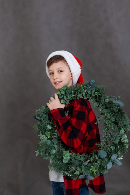 Porteiro de uma criança sorridente em uma camisa xadrez vermelha com uma guirlanda de Natal. Conceito de ano novo e boas festas.