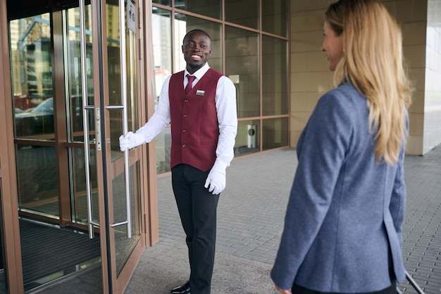 Porteiro sorridente do hotel abrindo a porta para os hóspedes do lado de fora