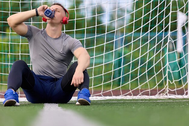 Foto el portero de fútbol se sienta en una superficie verde en el centro de la portería bebiendo agua de