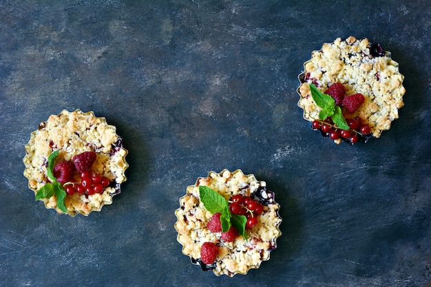 Portion Beerenkrümel knusprig in einer Auflaufform auf einem dunklen Hintergrund. Beerentörtchen mit Mürbeteig und saftiger Füllung. Leichtes Sommerdessert.