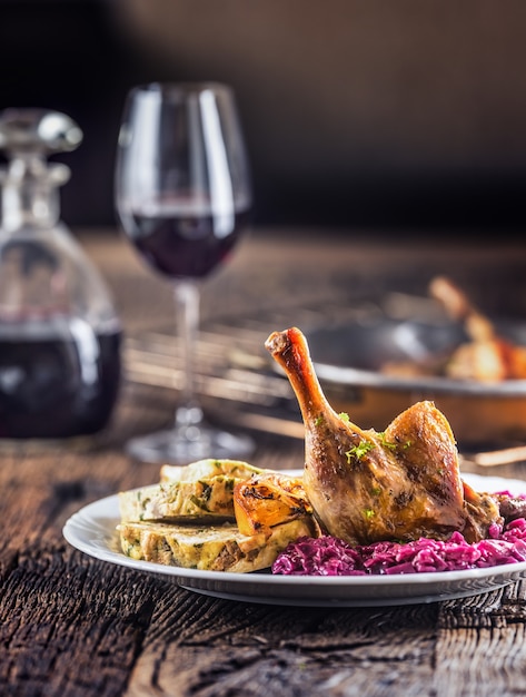 Portion gebratene Entenbein Rotkohl hausgemachte Knödel auf Teller und Rotwein auf dem Hintergrund.