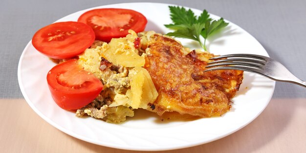 Portion kartoffelauflauf mit goldener fleischkruste auf teller mit frischen tomaten