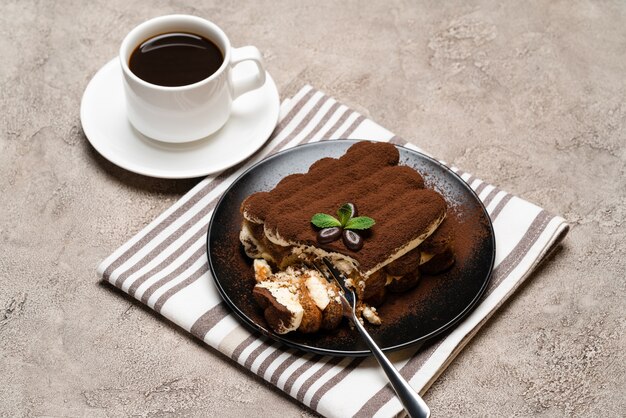 Portion klassisches Tiramisu-Dessert und Tasse frischen Espressokaffee auf Betonhintergrund