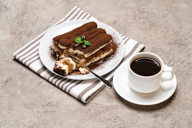 Portion klassisches Tiramisu-Dessert und Tasse frischen Espressokaffee auf Betonhintergrund