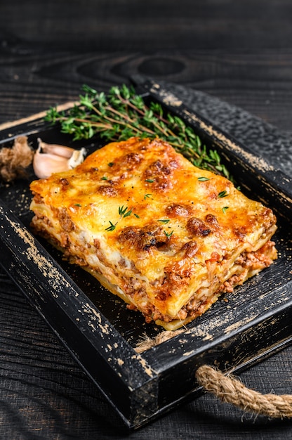 Portion Lasagne mit Hackfleisch und Tomaten-Bolognese-Sauce in einem Holztablett