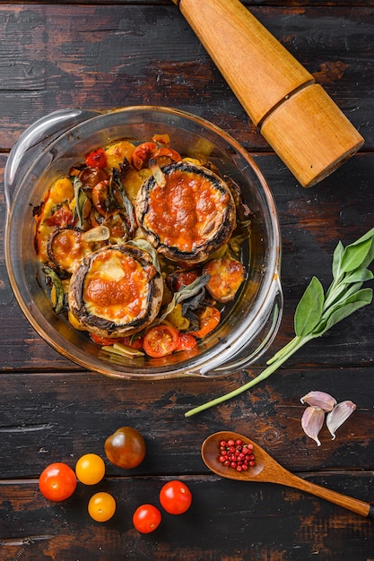 Portobello gebacken mit Cheddar-Käse, Kirschtomaten und Salbei im Glastopf auf alter hölzerner Hintergrundoberansicht.