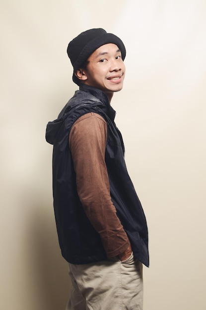 Porträt asiatischer Jugendlicher in cooler Pose mit Hut, braunem T-Shirt und schwarzer Weste, isoliert auf dem Hintergrund