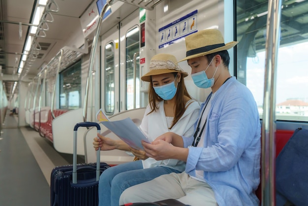 Porträt asiatischer Touristenpaare mit Maske, die im Skytrain in Bangkok, Thailand, die U-Bahn-Karte aus Papier zusammenhalten