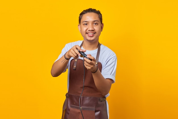 Porträt attraktiver und fröhlicher asiatischer junger Mann mit Schürze, der Spiel mit Joystick spielt