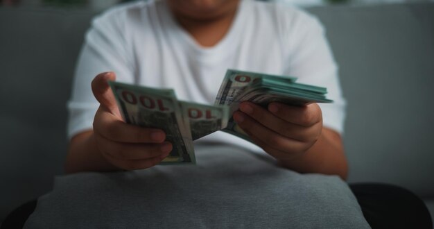 Porträt aus der Nähe Hände einer jungen asiatischen Frau genießen das Zählen von Bar-Dollar-Banknoten auf dem Sofa im Wohnzimmer zu Hause