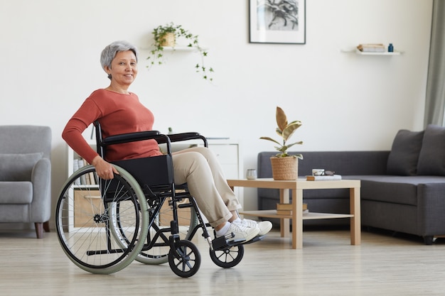 Porträt der älteren Frau, die im Rollstuhl sitzt und im Wohnzimmer zu Hause lächelt