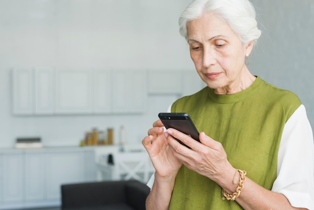 Foto porträt der älteren frau simsend am handy zu hause