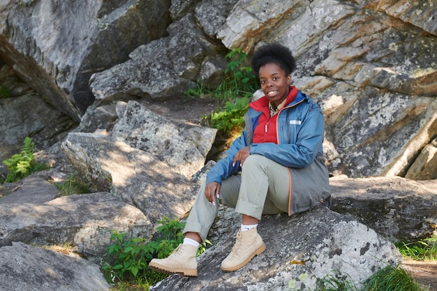 Porträt der afrikanischen Frau, die auf Felsen und während des Wanderns sitzt