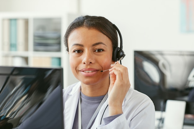 Porträt der afrikanischen jungen Frau im Kopfhörer, der vor Computer sitzt, der sie in einem Krankenwagen arbeitet