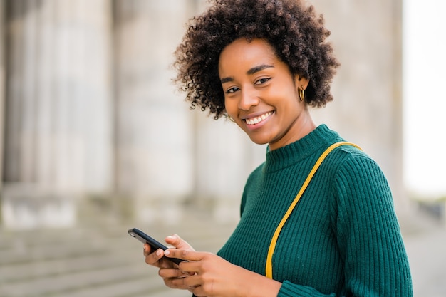 Porträt der Afro-Geschäftsfrau, die ihr Handy benutzt, während sie draußen auf der Straße steht. Geschäfts- und Stadtkonzept.