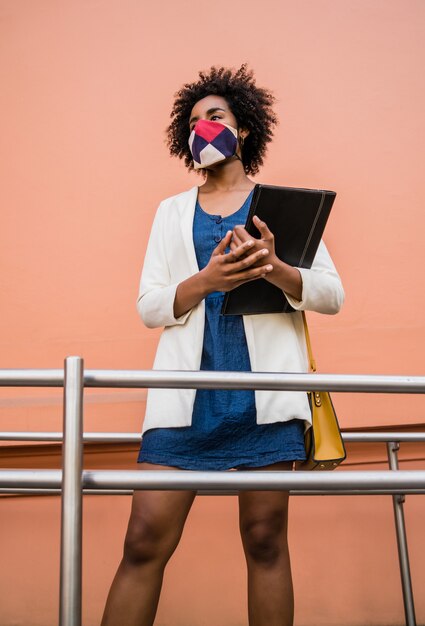 Porträt der Afro-Geschäftsfrau, die Schutzmaske trägt und ein Klemmbrett hält, während draußen an der Straße steht. Unternehmenskonzept.