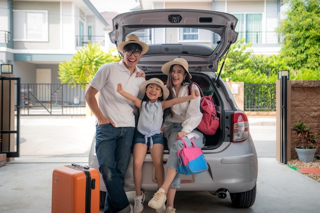 Porträt der asiatischen Familie mit Vater, Mutter und Tochter schaut beim Vorbereiten des Koffers in ein Auto für Feiertag glücklich.