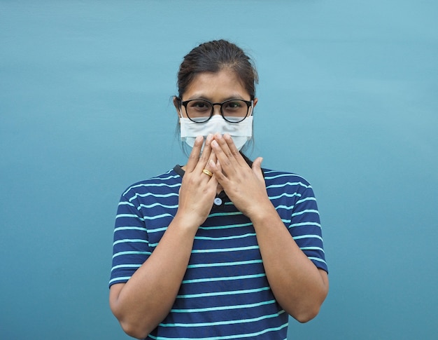 Porträt der asiatischen Frauen, die Brille und Schutzmasken tragen. Während er seinen Mund bedeckt Auf einem blauen Hintergrund