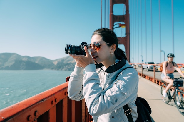 Porträt der asiatischen professionellen Fotografin fotografiert mit einer Digitalkamera auf der Golden Gate Bridge in San Francisco, Kalifornien, USA, in der Sonne.