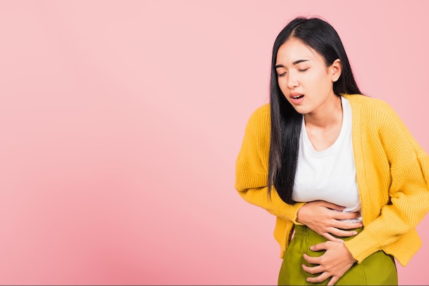 Porträt der asiatischen schönen jungen Frau hat Bauchschmerzen, weibliche Bauchschmerzen, die an Bauchschmerzen leiden, Studioaufnahme isoliert auf rosa Hintergrund, Gesundheits- und medizinisches Gastritis-Konzept