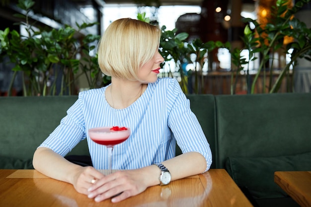 Foto porträt der attraktiven jungen frau, die cocktail im innencafé trinkt schöne blonde frau, die an der bar sich entspannt und einen cocktail trinkt