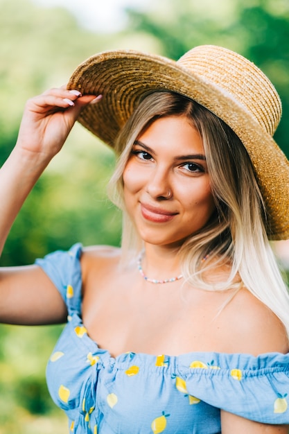 Porträt der attraktiven jungen Frau im Strohhut draußen am sonnigen Sommertag.