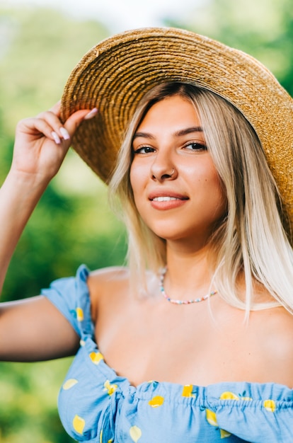 Porträt der attraktiven jungen Frau im Strohhut draußen am sonnigen Sommertag.