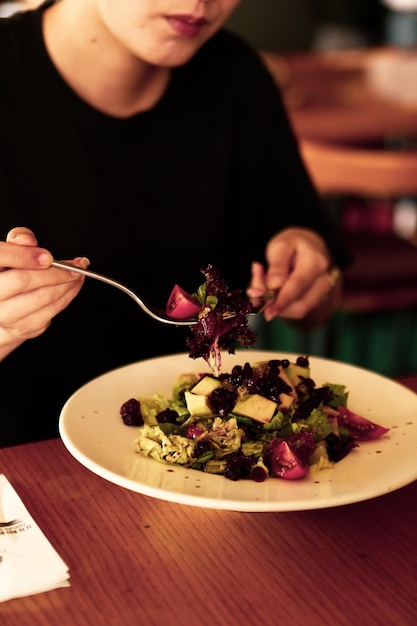 Porträt der attraktiven kaukasischen lächelnden Frau, die Salatfokus auf Hand und Gabel isst