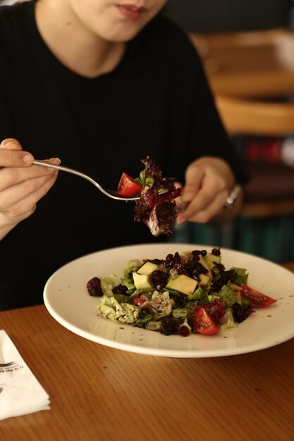 Porträt der attraktiven kaukasischen lächelnden Frau, die Salatfokus auf Hand und Gabel isst