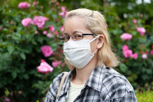 Porträt der blonden Frau der gemischten Rasse mittleren Alters mit Brille, die weiße chirurgische Maske trägt