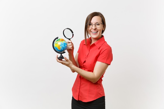 Porträt der Business-Lehrer-Frau im roten Hemd hält und schaut durch die Lupe auf dem Globus isoliert auf weißem Hintergrund. Bildungsunterricht im Hochschulkonzept. Platz kopieren.
