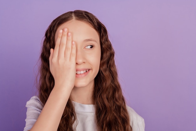 Porträt der charmanten hübschen kleinen dame palm verstecken halbes gesicht auge blick seitlich leeren raum auf violettem hintergrund