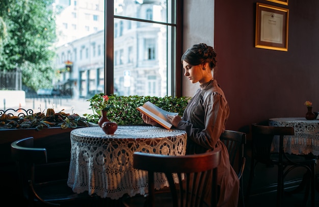 Porträt der Dame im Café, das Buch nahe Fenster liest