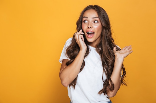 Porträt der europäischen Frau 20s mit langen Haaren, die auf Handy schreien und sprechen, lokalisiert über gelber Wand