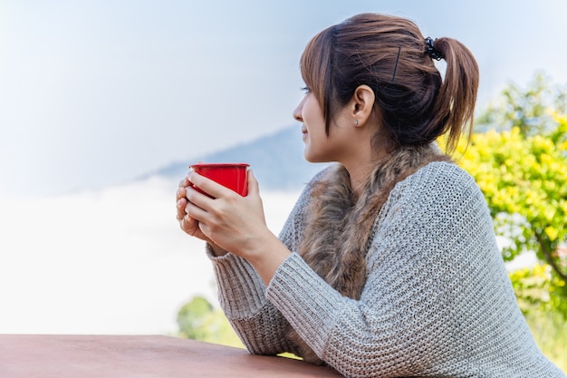 Porträt der Frau die warme Kleidung tragend, die den Becher Kaffee draußen genießt Nebelbergblick hält.