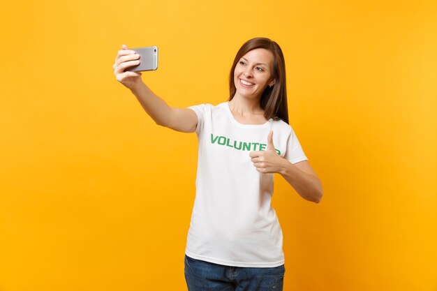 Porträt der Frau im weißen T-Shirt geschrieben Inschrift grüner Titel Freiwilliger, der selfie auf dem Handy auf gelbem Hintergrund schoss. Freiwillige kostenlose Hilfe hilft Konzept für Wohltätigkeitsarbeit