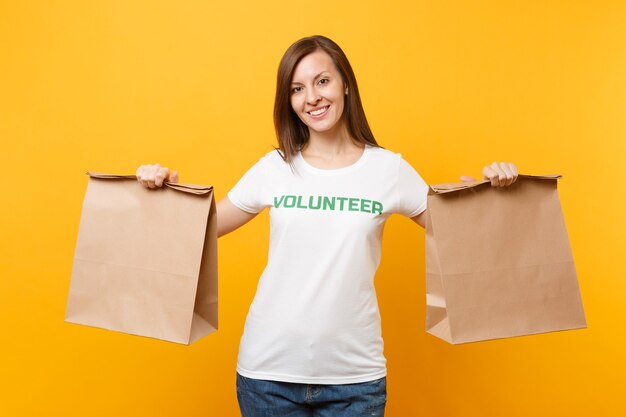 Porträt der Frau im weißen T-Shirt geschrieben Inschrift grüner Titel Freiwilliger halten leere Handwerkspapiertüte zum Mitnehmen isoliert auf gelbem Hintergrund. Freiwillige kostenlose Hilfe hilft Konzept der Nächstenliebe