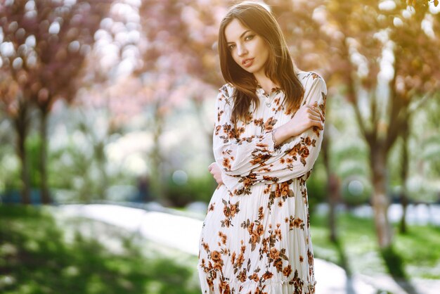 Porträt der Frau in einem hübschen Kleid mit Blumen genießt blühenden grünen Garten im Frühlingstag. Mode- und Stilkonzept.