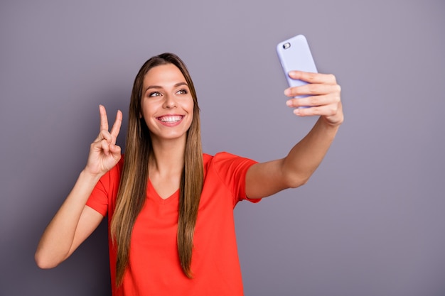 Porträt der fröhlichen brünetten Dame im roten T-Shirt, das gegen die lila Wand mit Telefon aufwirft