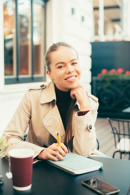 Porträt der fröhlichen jungen frau, die im café sitzt und zeit hat, um tasse tee zu trinken